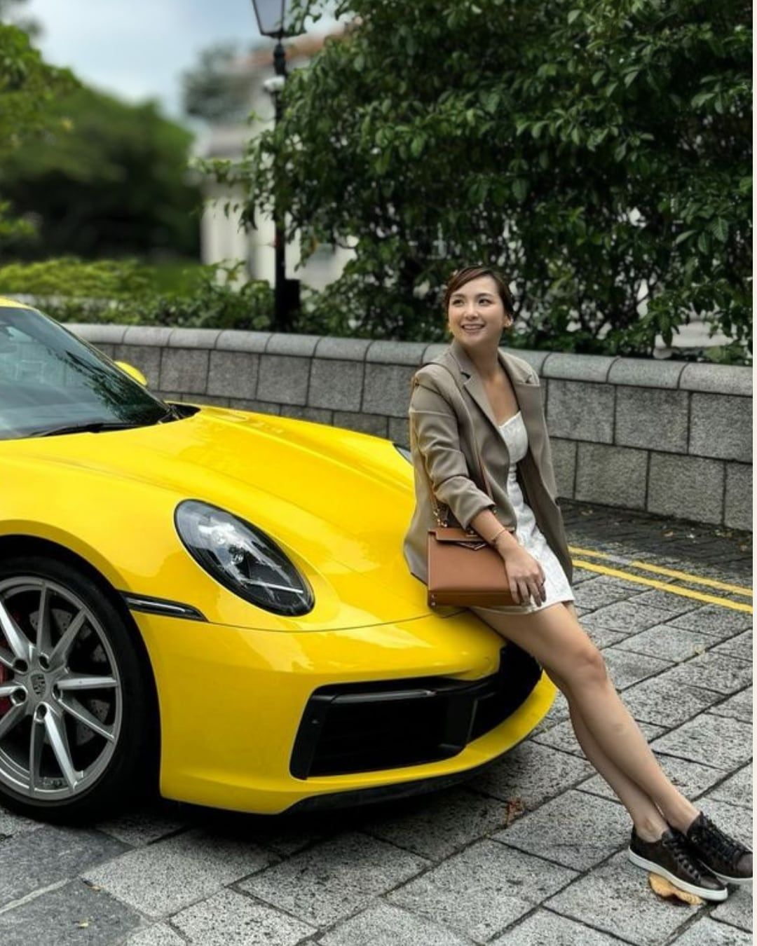 A client sitting on the bonnet of a yellow sports car, smiling.