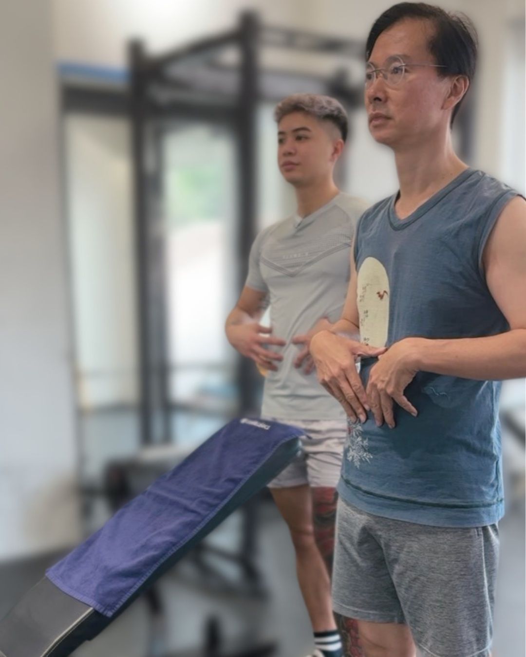 Fred and a client standing side by side, both hands on their stomachs, practising a brace.