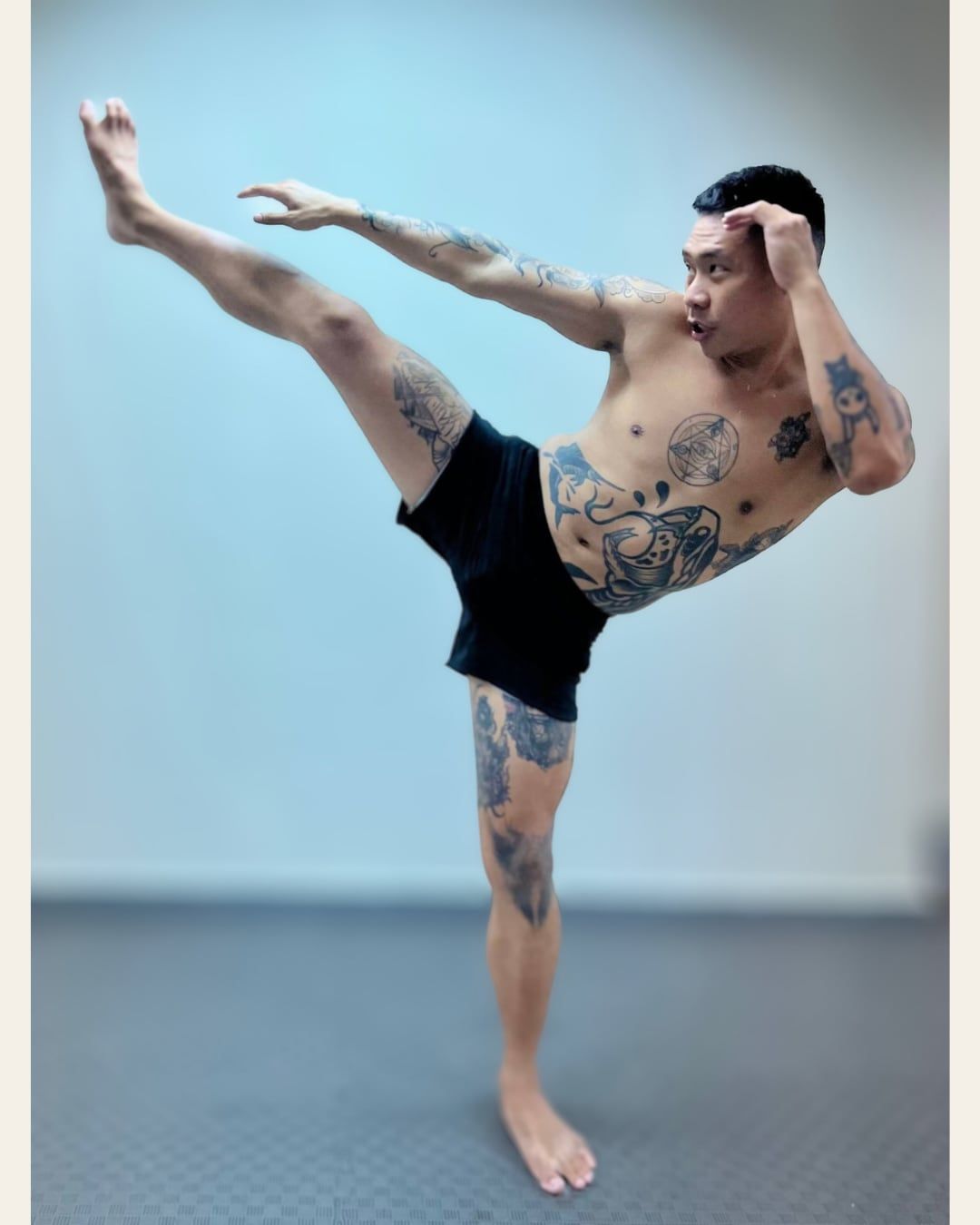 A client holding a high roundhouse kick, barefoot on a mat, background blurred.