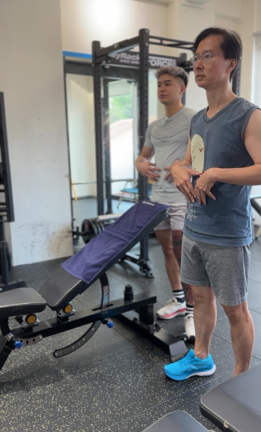 Fred coaching from the background as a client learns to brace his core through a movement.