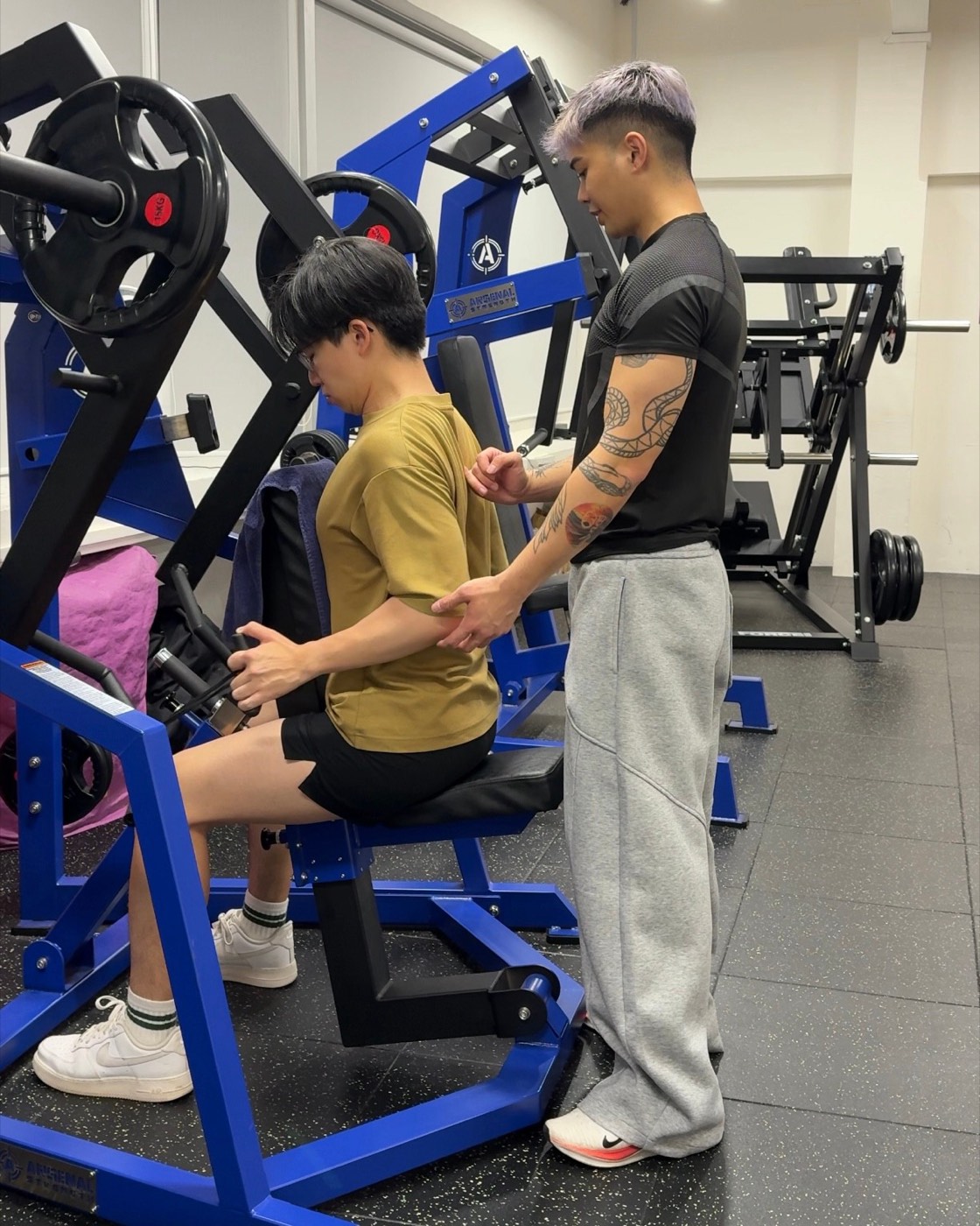 Fred standing behind a client on a machine row, cueing the lats and mid-back with touch.
